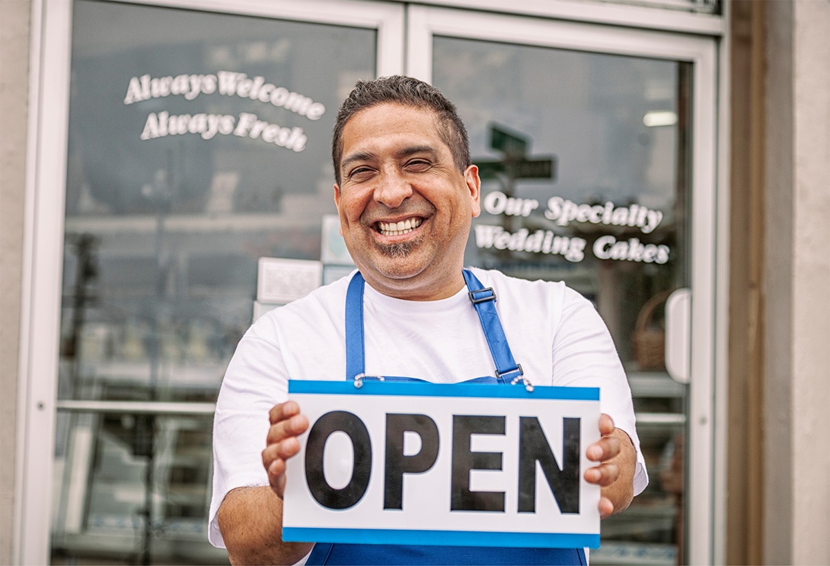 Small business owner smiling and holding a sign that says "open".
